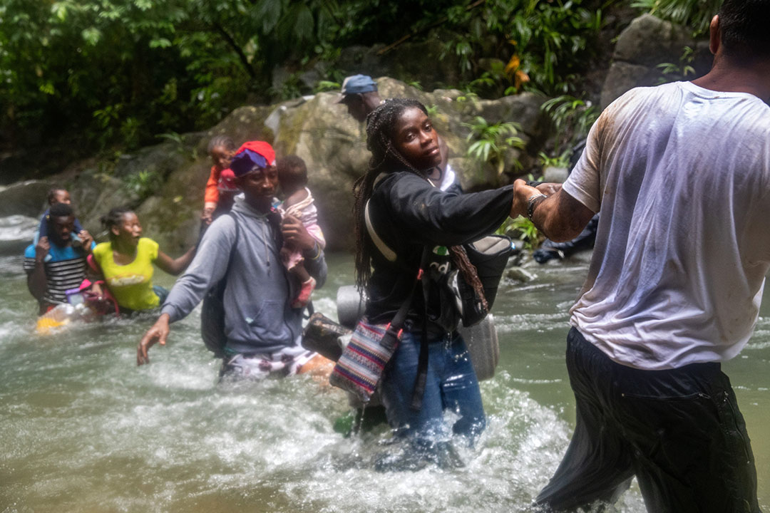 A Haitian man helps a Haitian woman cross a river, in company of other Haitian migrants.